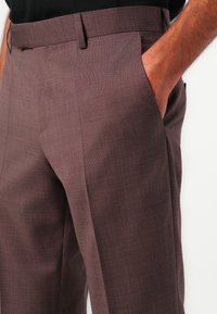Pantaloni tailored bordeaux scuri in un tessuto strutturato, con tasche laterali e una vita aderente. Motivo a righe sottili.