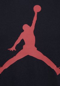 T-shirt en tissu noir arborant une grande silhouette rouge d'une personne sautant pour tirer au basket, mettant en avant le mouvement athlétique et le design.