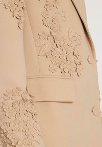 Blazer bej, croit cu detalii de aplicații florale pe mâneci și pe față, cu o formă structurată, închis cu un singur nasture și buzunar tip patch.