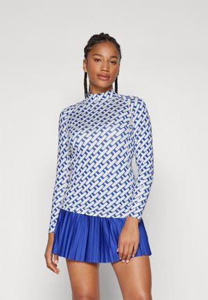 Long-sleeve shirt in white print with blue geometric pattern, paired with a pleated blue skirt. Both feature smooth, stretchy fabric.