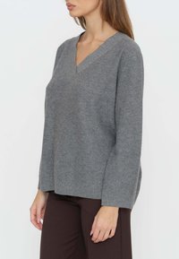 Maglione grigio a scollo a V realizzato in tessuto morbido, con maniche lunghe e vestibilità ampia, finitura strutturata e dettagli a costine sull'orlo.