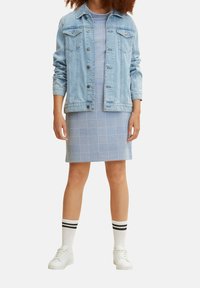 Chaqueta de mezclilla azul claro con mangas largas sobre un vestido ajustado de cuadros en tonos azules, combinada con zapatillas blancas y calcetas a rayas.