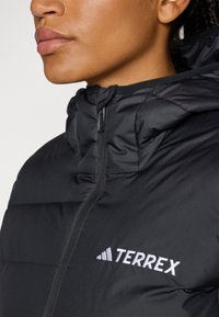 Black insulated jacket with a high collar and zip closure. Features a white "TERREX" logo on the left side. Smooth texture.