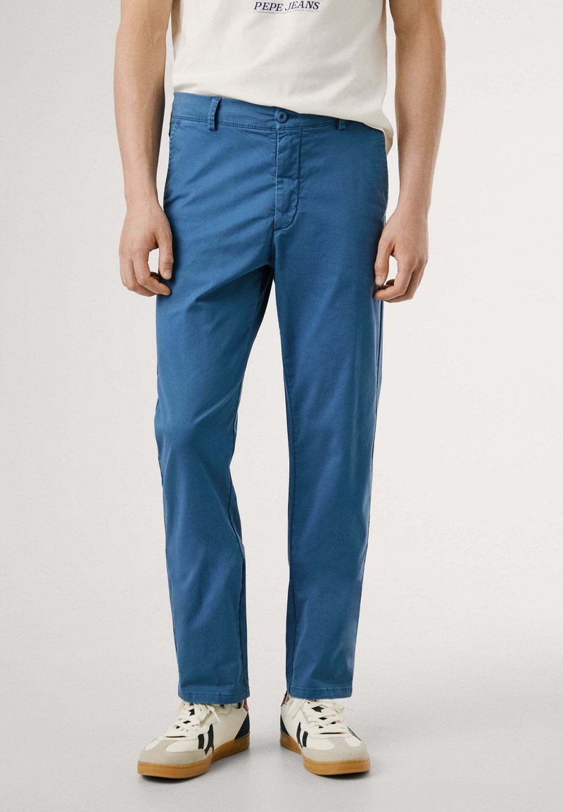 Chinos en coton bleu ciel avec une coupe droite, dotés d'une fermeture par bouton, d'une braguette zippée et de poches latérales, associés à des baskets blanches et beiges.