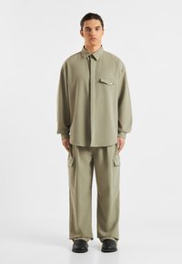 Lys olivengrøn outfit bestående af en langærmet skjorte med knapper og brystlomme samt brede cargo-bukser med sidelommer. Glat stof.