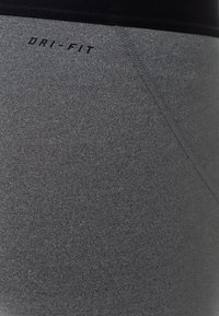 Zbliżenie szarego elastycznego materiału z detalami szwów i napisem "DRI-FIT" w kolorze czarnym blisko górnej krawędzi.