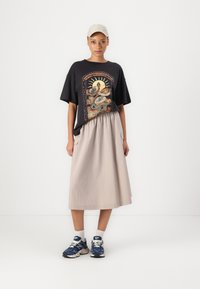 Svart grafisk t-skjorte med slangedesign, kombinert med en beige, knelang skjørt med sidelommer. Brukt med blå sneakers.