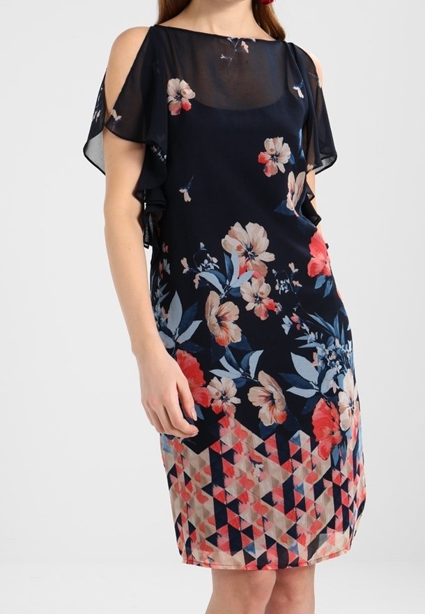 Kukallinen mekko, jossa on syvän sininen tausta, läpikuultavat kyljistä avonaiset hihat ja geometrisesti kuvioitu helma punaisen, vaaleanpunaisen ja beigen sävyissä.