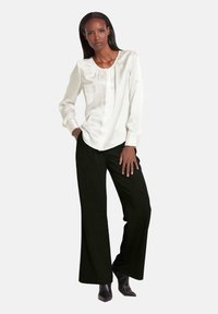 Witte zijden blouse met geplooide halslijn, lange mouwen, gecombineerd met zwarte wijde broek en puntige zwarte enkellaarsjes.