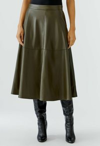 Jupe midi en cuir vert olive avec une taille cintrée, un ourlet évasé et un léger éclat. Associée à des bottes noires montantes.