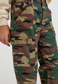 Camouflage cargobroek in groen, bruin en beige met meerdere zakken en een stevige katoenen textuur. Details omvatten drukknopen.