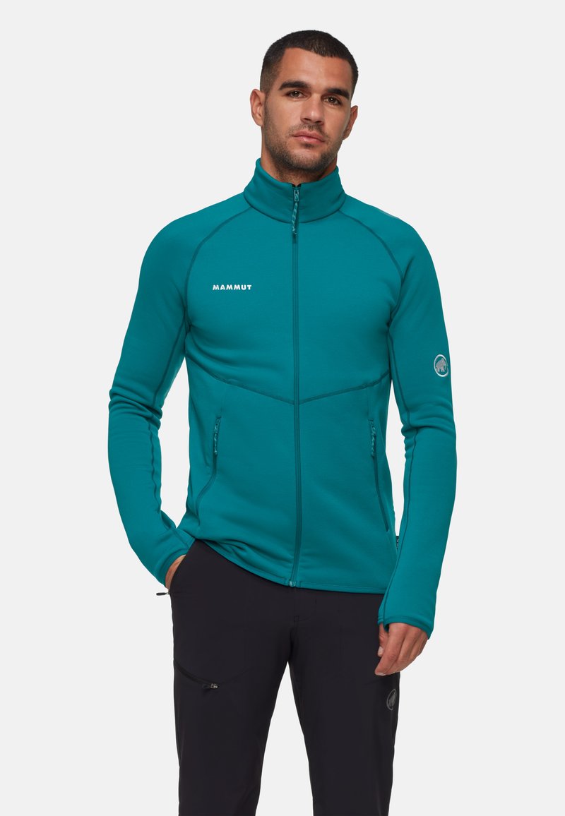 Teal fleecejack met een hoge kraag, ritsluiting en twee zijzakken met rits. Heeft contrasterende stiksels en een logo op de borst.