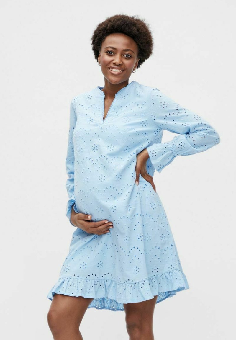 Šviesiai mėlyna suknelė su akytuoju siuvinėjimu, raukšlėtu apvadu ir ilgomis rankovėmis. Yra atlenktas apykaklė ir laisvas kirpimas, užtikrinantis komfortą.