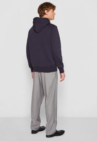 Sweat à capuche bleu marine avec une texture subtile, poche kangourou et cordon de serrage ajustable. Associé à un pantalon plissé gris clair et des chaussures noires.