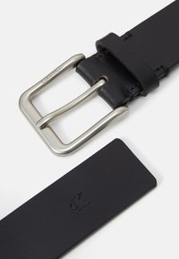 Black leather belt featuring a silver metallic buckle, with a stamped "CK" logo on a flat end. Smooth texture with clean lines.
