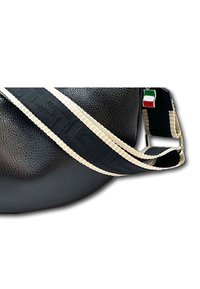 Zwarte leren tas met een textuur, voorzien van een geweven zwart en crèmekleurige schouderband met een patroon, en een klein Italiaans vlaggetje als bedel.