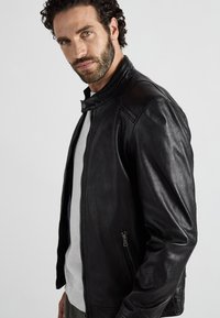 Zwarte leren motorjack met hoge kraag, ritszakken opzij en een gladde textuur. Draag het over een grijze trui met ronde hals.