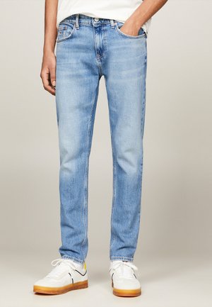 Jeans in denim azzurro chiaro con vestibilità dritta, design a cinque tasche e cuciture a contrasto. Abbinati a sneaker bianche con dettagli gialli.