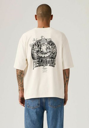 Cream-colored oversized t-shirt with a black graphic design featuring flowers and a mushroom on the back. Short sleeves, cotton material.