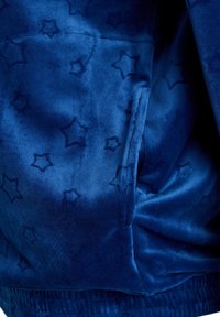 Blauer Samtstoff mit einem dezenten Sternenmuster und glatter Textur. Enthält eine in das Design integrierte Tasche.