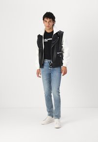 Black leather and white fleece hybrid jacket, black t-shirt, light blue jeans, and white sneakers. Striking design with zip and button details.