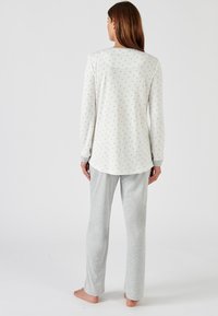 Long-sleeve, cream pajama top with small floral print; gray, soft fabric pants with a straight leg design. Suitable for loungewear.