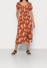 Robe midi couleur rouille avec manches bouffantes, imprime floral et décolleté en forme de clé. Le matériau suggère un tissu léger ; poches incluses.