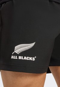 Zwarte sportshorts van textuurstof met een wit varenlogo en de tekst "ALL BLACKS" aan de onderste linkerkant.