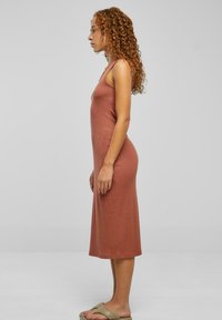 Rochie midi ribbed în terracotă, fără mâneci, cu o siluetă ajustată. Dispune de o culoare solidă, o textură moale și un tiv până la glezne.