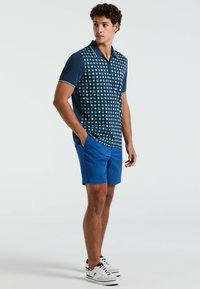 Polo bleu marine avec un motif géométrique en bleu clair, associé à un short bleu uni. Il présente un col classique et des manches courtes.