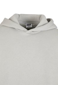 Ljust grå hoodie med nedfällt huva som visar inre etikett med texten "Urban Classics M Tillverkad i Kina."