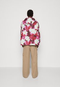 Colorful puffer jacket with a floral pattern in pink, white, and green, featuring a hood and loose fit, paired with beige cargo pants.