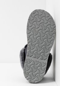 Sål af en grå Birkenstock-sko med bølgende mønster og "Birk" tekst, der viser blødt sort pelsfor rundt om kanten.
