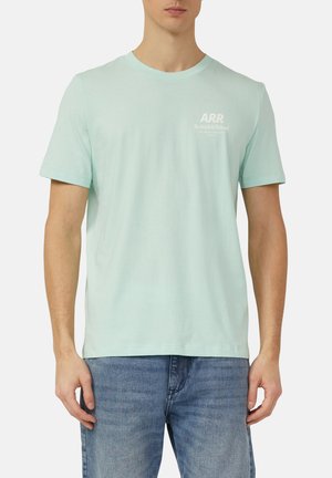 Mann trägt ein hellgrünes kurzärmeliges T-Shirt mit kleinem weißen "ARR Rethink&Reload"-Text auf der Brust und blaue Jeans vor weißem Hintergrund.