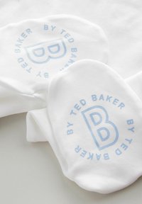 Fehér pamut ruházat, világoskék kör alakú logóval, melyen 'B' és a 'BY TED BAKER' felirat található. Puha tapintású, kerek formájú és tiszta kidolgozású.