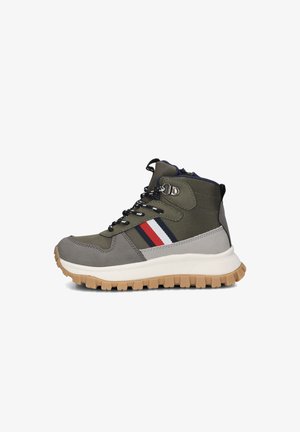 Hikingboots geïnspireerd door herenmode, gemaakt van olijfgroen synthetisch materiaal met grijze accenten, een witte zool en een rood/blauw gestreept detail aan de zijkant.