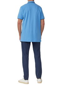 Lichtblauw polo-shirt met marineblauwe accenten, gecombineerd met donkere broek en witte sneakers, vanuit achteraanzicht en in een ontspannen pasvorm.