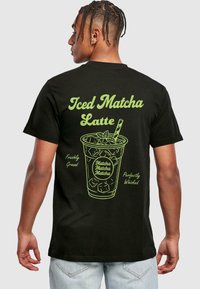 Black t-shirt featuring a green graphic of an iced matcha latte with text: "Iced Matcha Latte," "Freshly Ground," and "Perfectly Whisked."