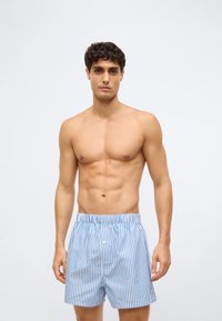 Μπλε και λευκές ριγέ μποξεράκια από ελαφρύ ύφασμα με ελαστική ζώνη και μία κουμπί μπροστά.