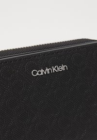 Czarny portfel teksturowany z zamkiem błyskawicznym, z wypukłym wzorem i srebrnym logo Calvin Klein z przodu.