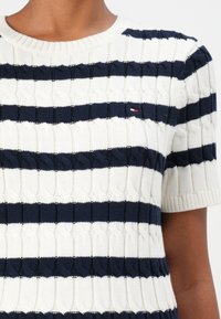 Kurzärmliger Strickpullover mit navyfarbenen und weißen horizontalen Streifen, strukturiertem Kabeldesign und kleinem Logo auf der linken Brust.