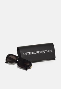 Mustad ristkülikukujulised prillid tumedate läätsede ja tekstuurse raami ning musta kõva karbiga, millel on valged tähestikud "RETROSUPERFUTURE."