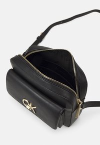 Černá kožená crossbody taška se zlatým zipem a kovovými detaily. Obsahuje kapsu na přední straně s klopou a několik vnitřních přihrádek.