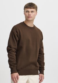 Brun bomullgenser med rund hals, ribbestrikkede mansjetter og hem. Har en avslappet passform og teksturert stoff.