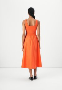 Orange sleeveless dress with square neckline, fitted bodice, and flared skirt. Made of lightweight fabric, worn with black shoes.