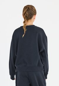 Överdimensionerad svart sweatshirt med mjuk textur, ribbade ärmslut och rund halsringning. Har en avslappnad passform och sömlös axeldesign.