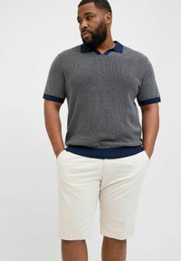 Kortærmet polo striktrøje i mørkegrå med marineblå krave og manchetter, parret med lysebeige shorts med lommer, afslappet pasform.