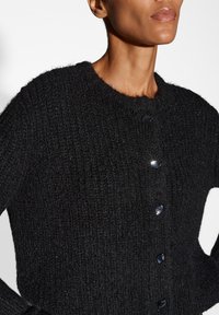 Schwarze Strickjacke mit strukturiertem Oberflächenmaterial, Rundhalsausschnitt und fünf glänzenden Knöpfen auf der Vorderseite.