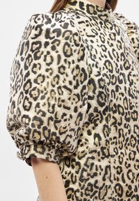 Bluzka w panterkę wykonana z fakturowanego materiału, z krótkimi bufiastymi rękawami, wysokim kołnierzem i ozdobnym elementem na mankiecie.