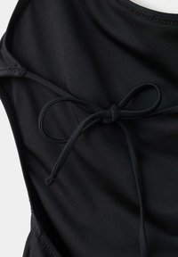 Vêtement noir avec un nœud noué fait à partir du même cordon en tissu, montrant une texture lisse et des bords cousus.